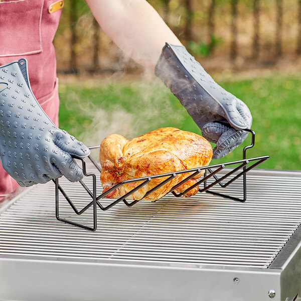 A person using a Fox Run non-stick roasting rack to cook a chicken on a grill.