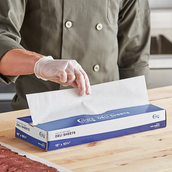 A person in gloves holding a white and blue box of Choice Interfolded Deli Wrap Wax Paper.