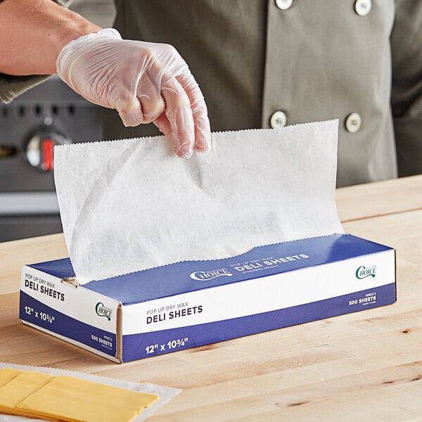 A person wearing gloves using Choice white and blue customizable interfolded deli wax paper to wrap food.