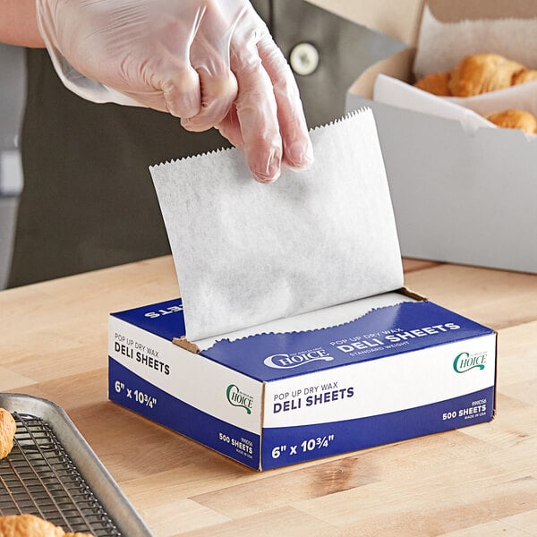 A hand using Choice interfolded wax paper to put doughnuts in a blue and white box.