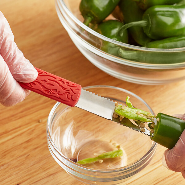 A person using an Outset stainless steel jalapeno corer with a red handle to core a green pepper.