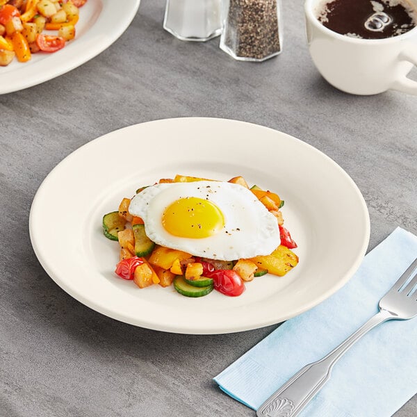 A plate of food with a fried egg and vegetables on an Acopa Ivory stoneware plate.