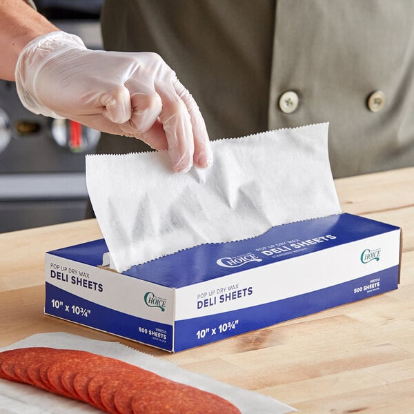 A person wearing gloves holding a white box of Choice interfolded deli wrap paper.