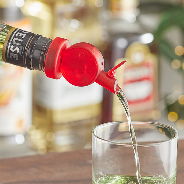 A Franmara transparent red speed pourer on a bottle pouring liquid into a glass.