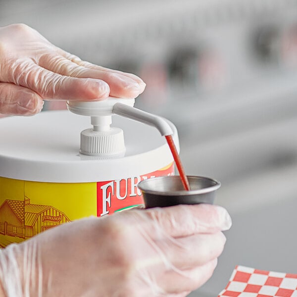 A person in gloves using a Carnival King plastic condiment pump to dispense liquid into a container.