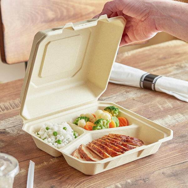 A hand holding a Tellus Products natural bagasse container of food.