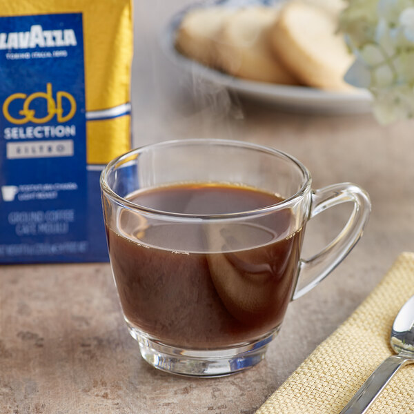 A glass cup of Lavazza Gold Selection Filtro Coarse Ground Coffee with a spoon on a table.