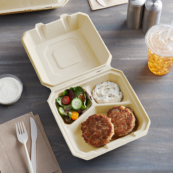 A Tellus Products natural bagasse clamshell container with 3 compartments filled with food on a table.
