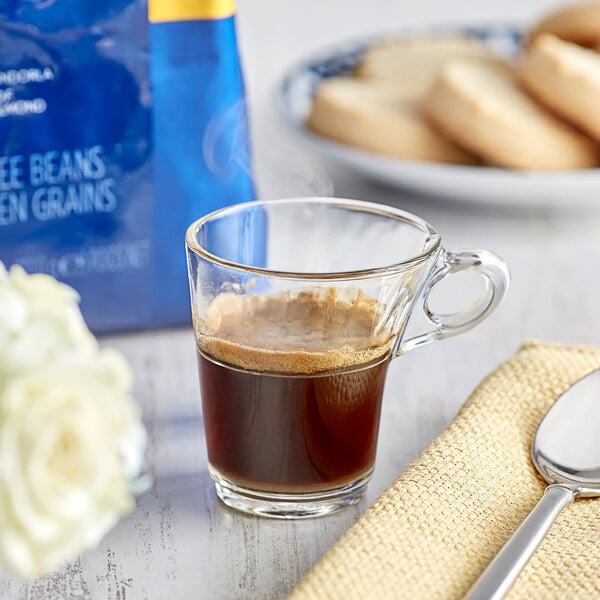 Lavazza Gold Selection Whole Bean Espresso in a glass cup of coffee with a spoon and a plate of cookies.