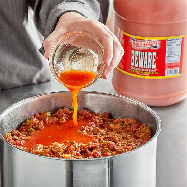 A person pouring Marie Sharp's Beware Comatose Habanero Hot Sauce into a pot.