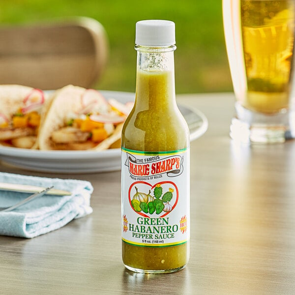 A bottle of Marie Sharp's green hot sauce on a table with a plate of food.
