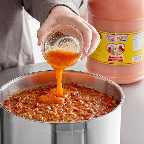 A person pouring Marie Sharp's Garlic Habanero hot sauce into a pot of food.