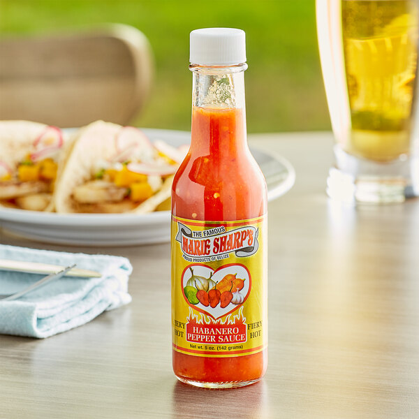 A bottle of Marie Sharp's Fiery Hot Habanero Hot Sauce on a table next to a plate of food.