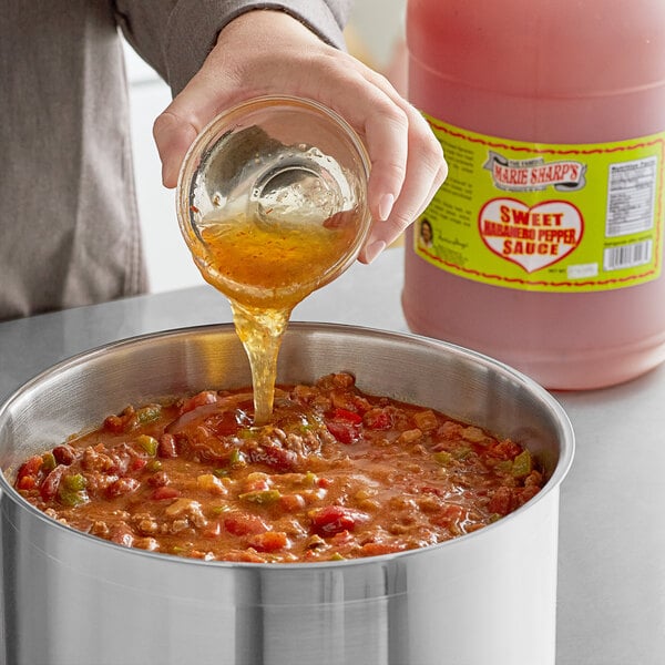 A person pouring Marie Sharp's Sweet Habanero Hot Sauce into a pot of food.