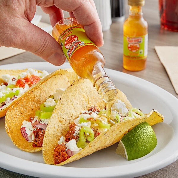 A hand pouring Marie Sharp's Sweet Habanero hot sauce into a taco shell.