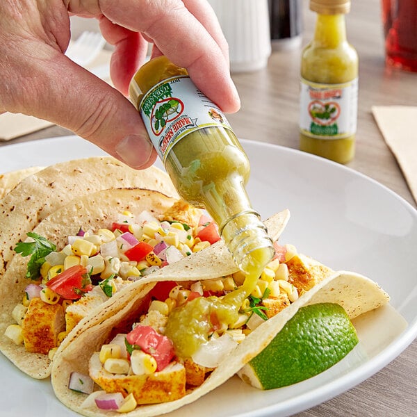 A person's hand pouring Marie Sharp's Green Habanero Hot Sauce onto a taco.