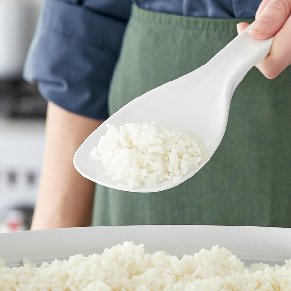 A person using a Choice solid plastic rice paddle to scoop rice into a bowl.