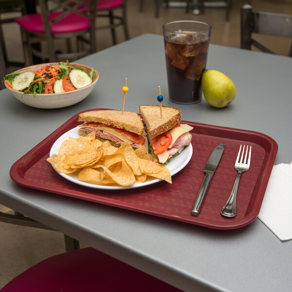 A Carlisle burgundy plastic fast food tray with a sandwich and chips on it.
