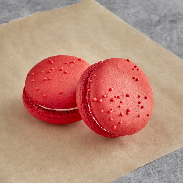 Two Macaron Centrale strawberry macarons on a brown surface.