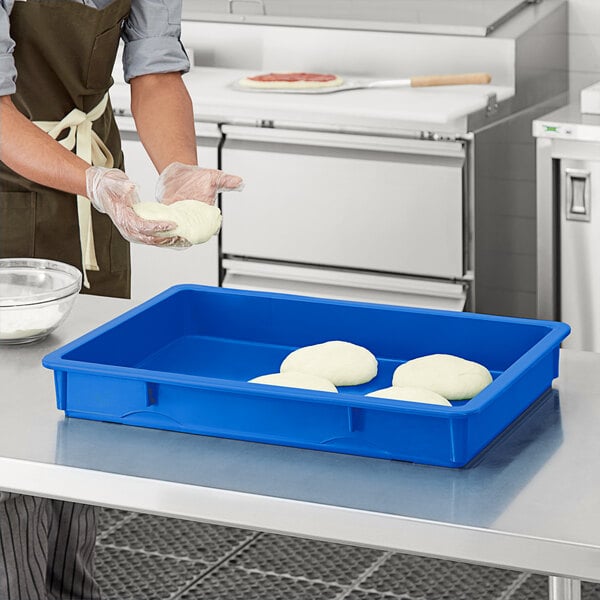 A person in a kitchen wearing gloves uses a blue Baker's Mark polypropylene dough proofing box to hold white dough.