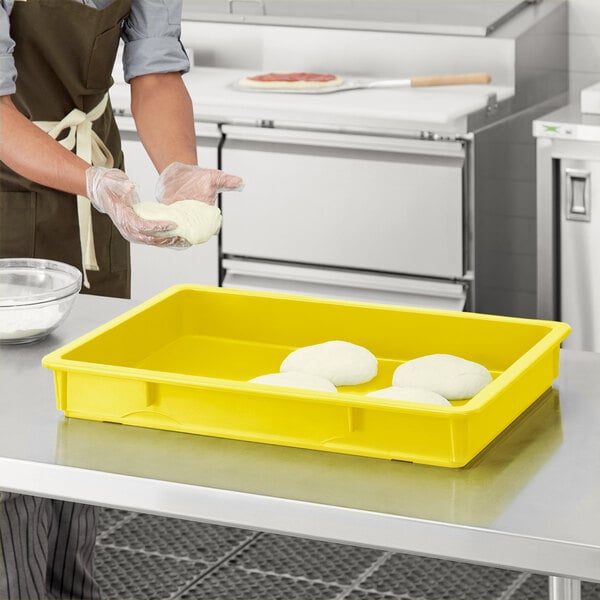 A person in a kitchen wearing gloves preparing dough in a yellow Baker's Mark polypropylene proofing box.