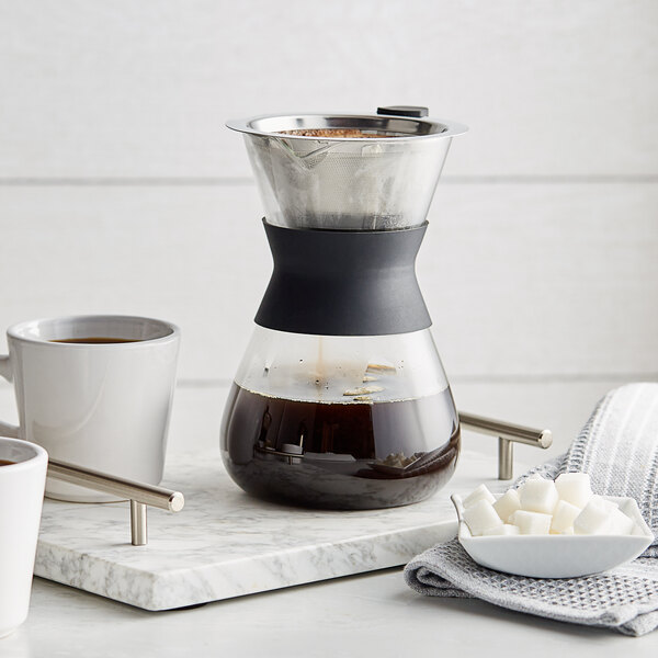An Acopa glass pour over coffee maker on a tray with cups of coffee.