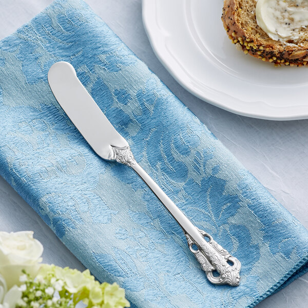 An Acopa Ophelia stainless steel butter knife on a blue napkin next to a plate of bread.