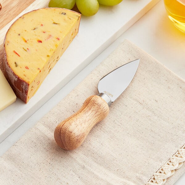An Acopa stainless steel cheese spade with a wooden handle next to cheese and grapes on a cutting board.