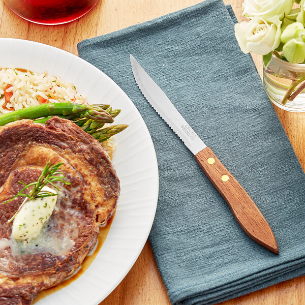 A plate of steak and asparagus with a Choice stainless steel steak knife with a natural wood handle.