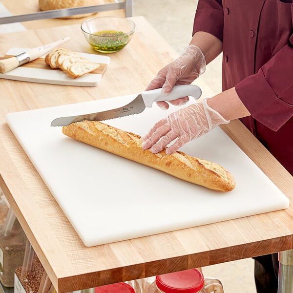A person in gloves cutting a loaf of bread on a white Choice cutting board.