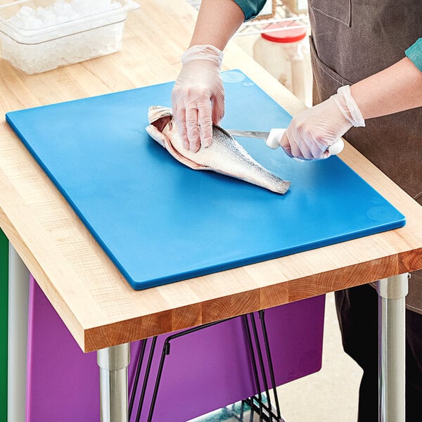 A person in gloves cutting a fish on a blue Choice polyethylene cutting board.