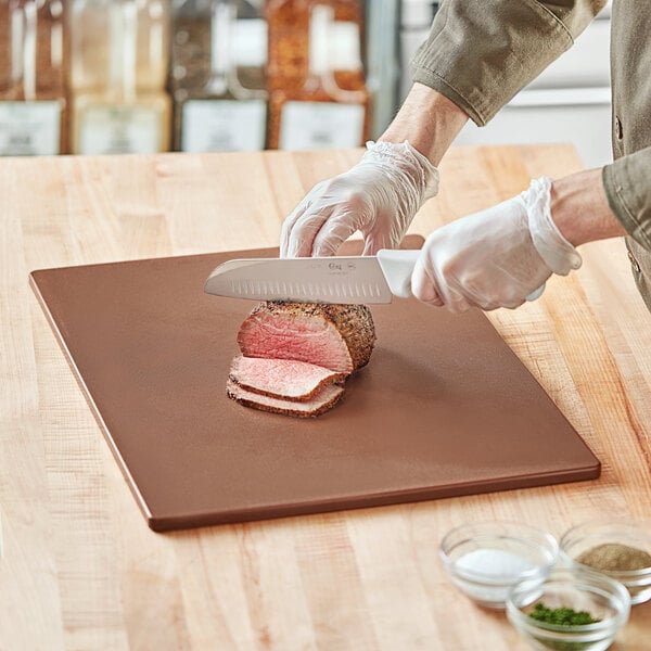 A person cutting meat on a brown Choice polyethylene cutting board.