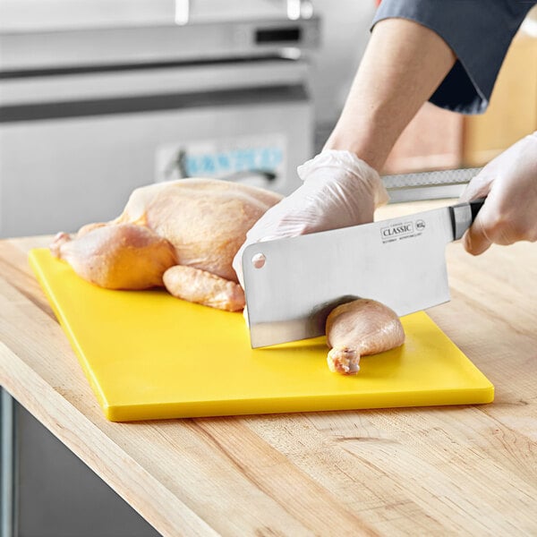 A person cutting a chicken on a yellow Choice polyethylene cutting board.