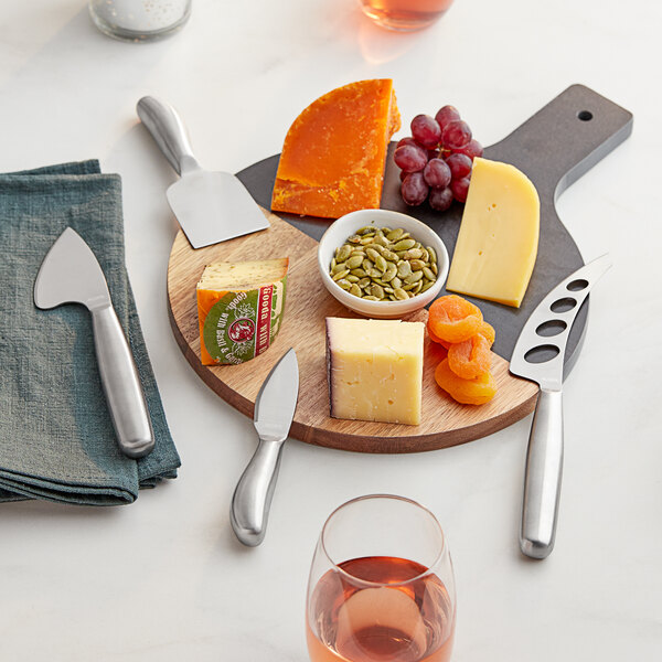 An Acopa stainless steel hard cheese knife set on a table with a cheese board with various types of cheese and fruits.