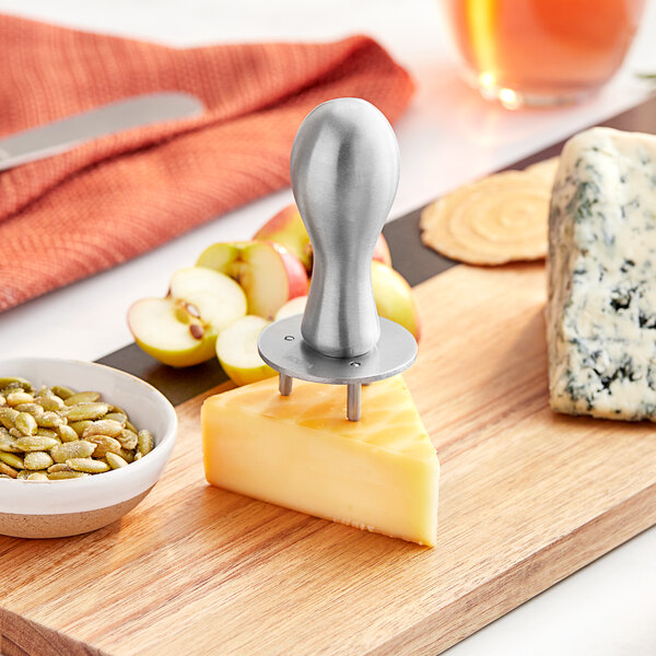 A stainless steel cheese button clincher in a block of cheese on a cutting board.