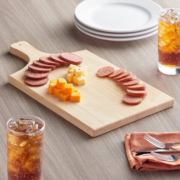 A Choice wooden serving and cutting board with sliced meat and cheese on it on a table.