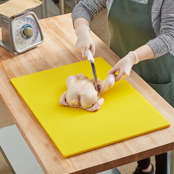 A woman cutting a chicken on a yellow polyethylene cutting board.