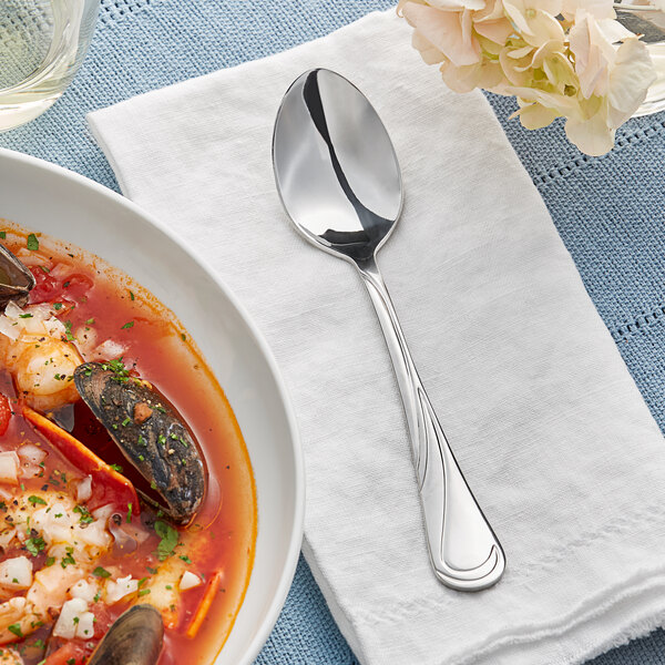 An Acopa stainless steel dinner spoon on a white napkin next to a bowl of soup with seafood.