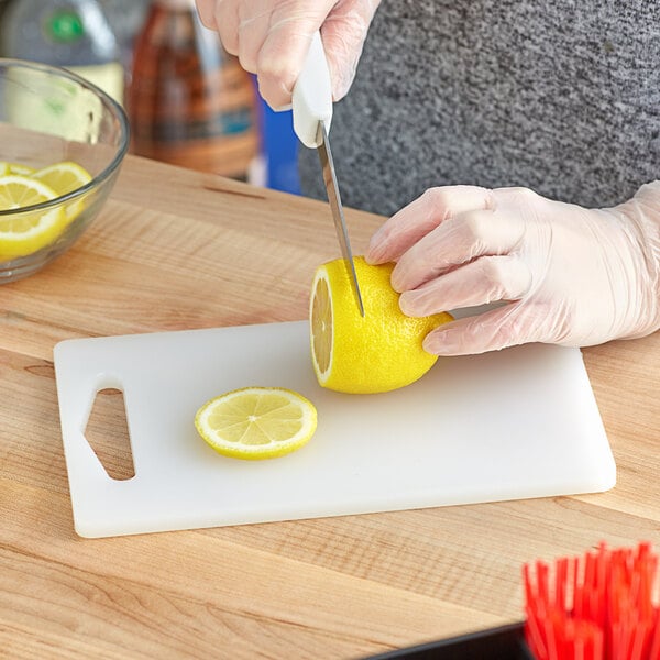 A person's hand with a Choice knife cutting a lemon on a Choice white polyethylene cutting board.