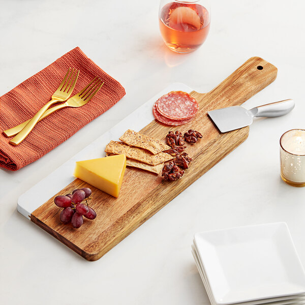 An Acopa acacia wood and marble serving board with food on it next to a fork and knife.