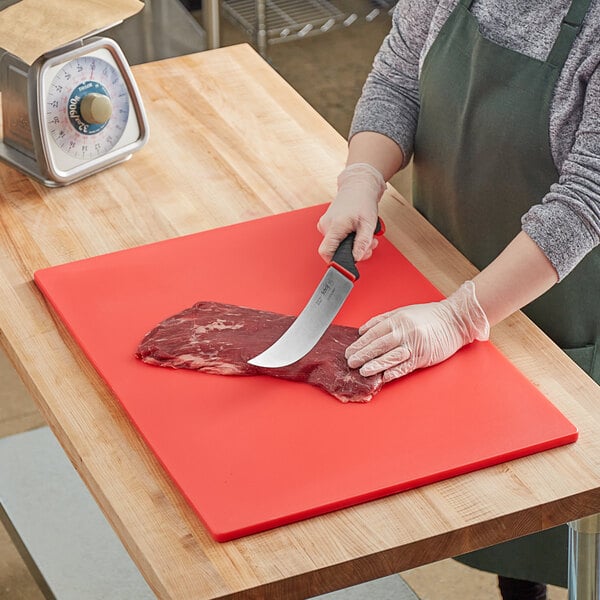 A woman wearing gloves cutting meat on a red Choice polyethylene cutting board.