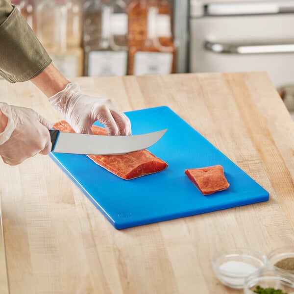 A person cutting raw salmon on a blue Choice cutting board.