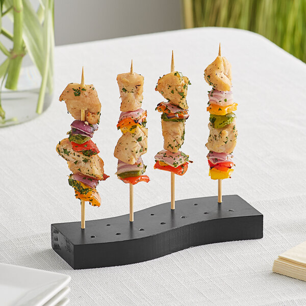 Acopa Mesa black wood skewer holder with chicken and vegetables on skewers on a table.