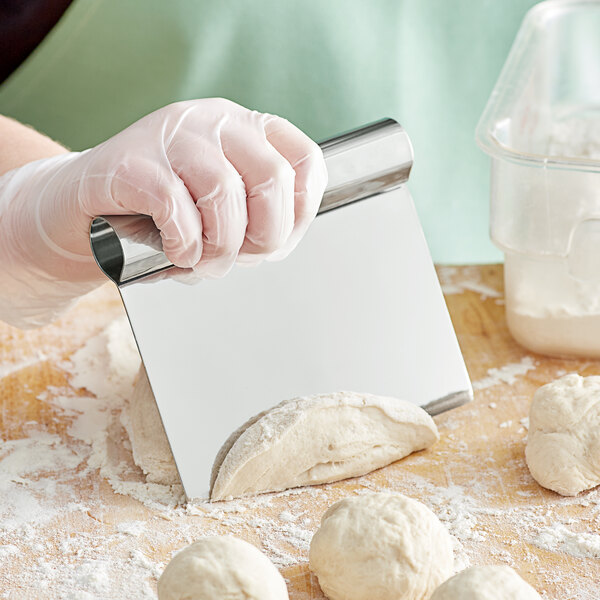 A person using a stainless steel dough cutter to cut dough on a table.
