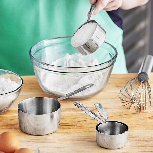 A woman using Choice stainless steel measuring cups to pour flour into a bowl.