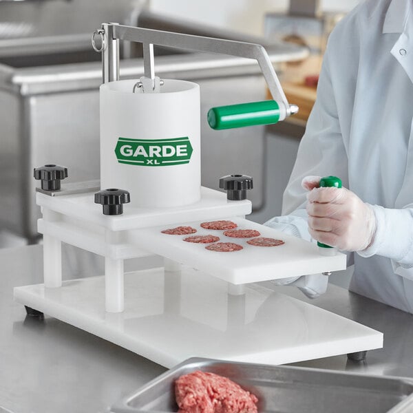A person in a white coat and gloves using a Garde XL slider press with a green handle on a counter.