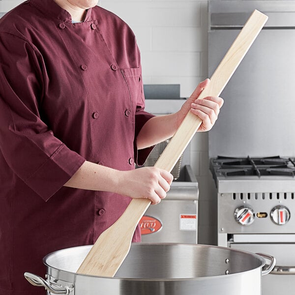 A woman in a chef's uniform stirring a pot with a Choice 36" wood paddle.