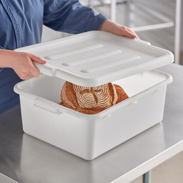 A person holding a white container with a loaf of bread inside.