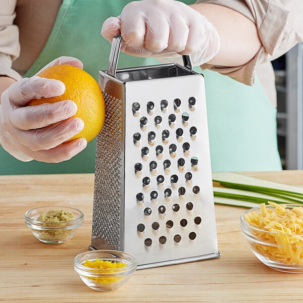 A person using a Choice stainless steel box grater to grate an orange.