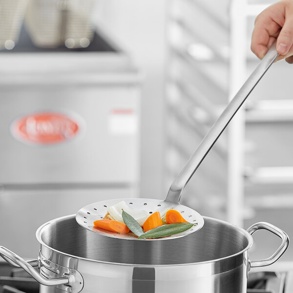 A person using a Choice stainless steel skimmer to stir vegetables in a pot.